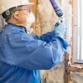 Rob Mages from the Green Jobs Corps uses spray foam to seal air leaks around a window. 